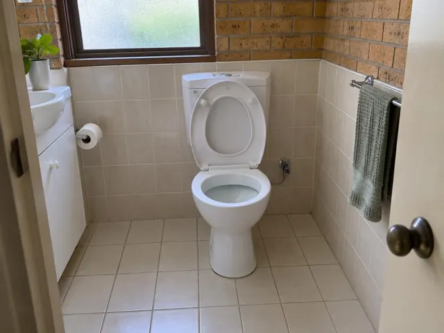 Clean white toilet in a tiled bathroom with beige walls and a window in Baulkham Hills