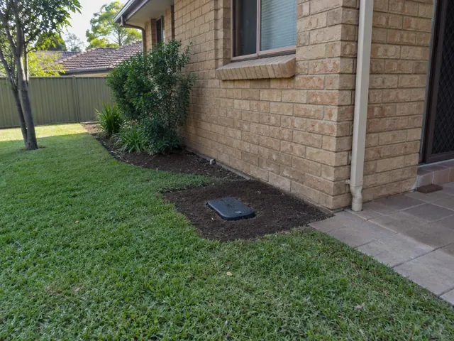 Capped sewer access cover in a tidy garden bed beside a brick house in Cherrybrook